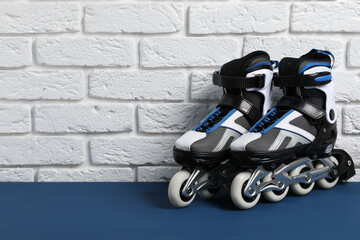 Pair of roller skates on blue table near white brick wall, space for text