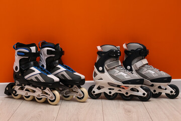 Pairs of roller skates on floor near orange wall