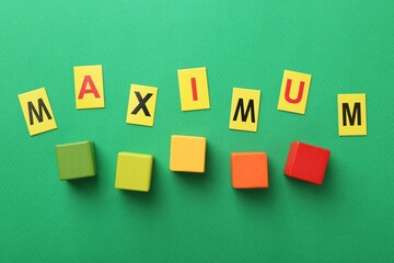 Word Maximum and colorful cubes on green background, flat lay