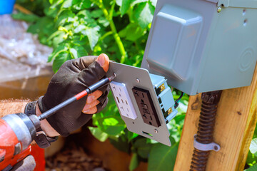 Homeowner works on installing an outdoor electrical outlet in garden during works day