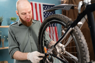 Bearded cyclist fixing bicycle wheel with wrench repairing and servicing bicycle at home DIY