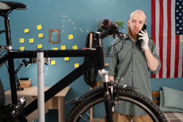 Bearded man fixing bicycle and using smartphone. Concept of maintenance bike