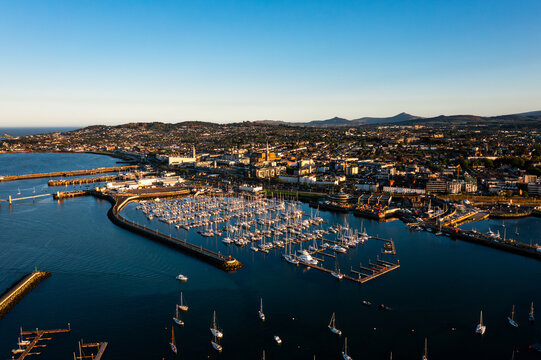 Aerial view of Dun Laoghaire Harbour with sailboats, town, and Dublin mountains during a glowing sunset