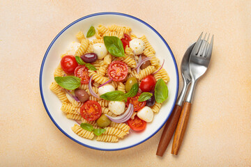 Plate with Italian fusilli pasta salad with fresh cherry tomatoes, mozzarella, olives, red onion, and basil leaves, concept of Italian culinary tradition