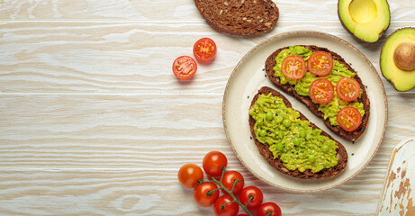 Slices of whole grain rye bread with mashed avocado, green peas and cherry tomatoes seasoned with black sesame seeds are served on a plate for a healthy breakfast or snack