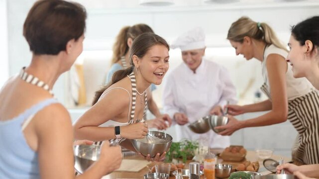  Young woman in apron learning to cook and chatting at cooking master class 
