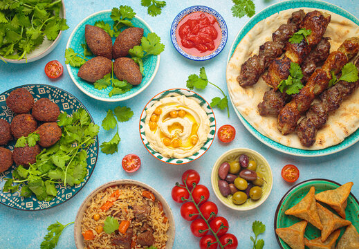 Top view of a vibrant table filled with lebanese dishes and mezze, featuring meat kebabs, falafel, kibbeh, hummus, sambousek, rice, olives. Middle eastern or Arab dishes