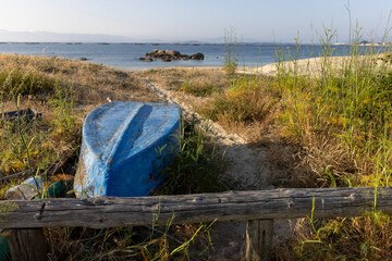 A blue boat is sitting on the beach next to a wooden bench. The scene is peaceful and serene, with...
