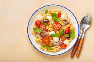 Plate with Italian fusilli pasta salad with fresh cherry tomatoes, mozzarella, olives, red onion, and basil leaves, concept of Italian culinary tradition