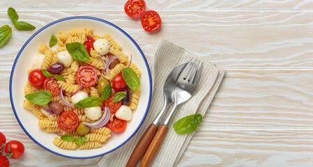 Plate with Italian fusilli pasta salad with fresh cherry tomatoes, mozzarella, olives, red onion,...
