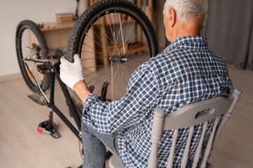 Elderly Man Fixing Bicycle Wheel Preparing Bike for Summer Season Indoors
