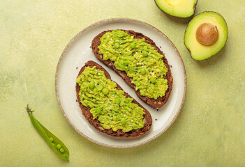 Two slices of toasted rye bread are topped with mashed avocado and sprinkled with sesame seeds, served on a plate, next to halved avocados, a healthy and vibrant breakfast or snack option