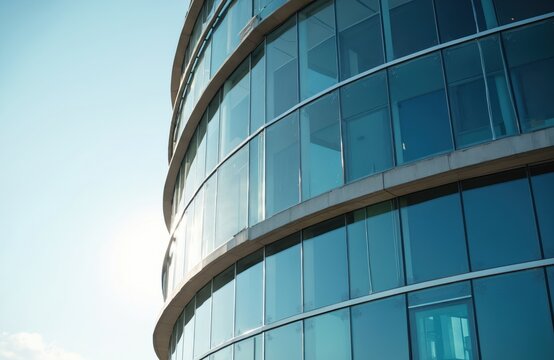 Modern office building with curved glass facade reflects sunlight. Contemporary architecture, glass walls create light reflections. Corporate urban design, business concept, high-rise structure,
