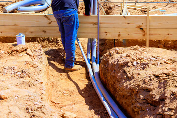 Male worker on installing grey electrical conduits at construction site surrounded by wooden...