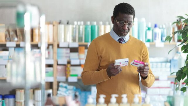 African man choose buy painkiller paracetamol tablet at pharmacy, compare with other good. Client check for absence of harmful substances, view product in details.