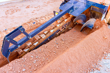 Heavy trencher equipment grinds through soil while preparing trench for underground utilities in an...