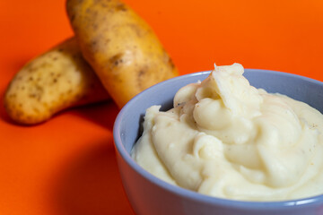 Mashed potatoes served in bowl with raw potatoes on orange background