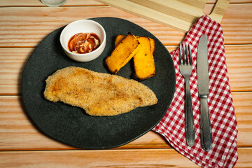 Breaded chicken breast with fried polenta and sauce on black plate