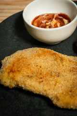 Breaded chicken cutlet with sauce on dark plate
