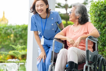smiling Asian caregiver in scrubs enjoys a moment outdoors with senior woman in a wheelchair,...