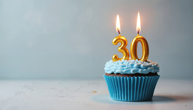 Festive birthday cupcake with gold number 30 candles. Blue frosted dessert on white marble surface. Anniversary celebration, party theme with candles in cake.