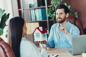 Real estate agent presenting housing model and keys while discussing property acquisition with...