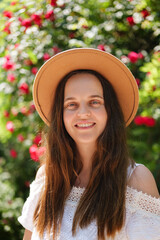 
A radiant young woman in a brown hat and white dress smiles directly at the camera, with a vibrant...