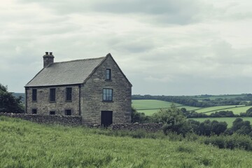 Obraz premium A charming rustic stone house is beautifully situated amidst the vibrant green countryside, surrounded by gentle rolling hills beneath a cloudy sky on a tranquil day