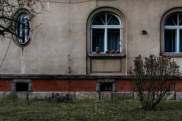 A simple residential building facade with two arched windows, decorative bars, and potted plants on...