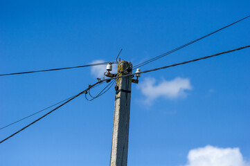a weathered utility pole supporting multiple power lines and electrical components against blue sky