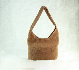 Knitted handmade milky brown bag on furry white blanket. 