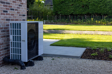 Quiet outdoor air-water heat pump unit near lush green garden and brick wall