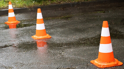 Road safety measures with bright cones marking wet pavement in an urban area during a rainy day