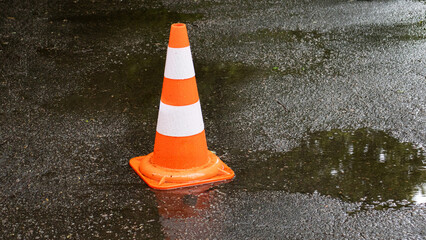 Bright orange traffic cone standing on a wet pavement reflecting the soft glow of rain in a quiet urban area