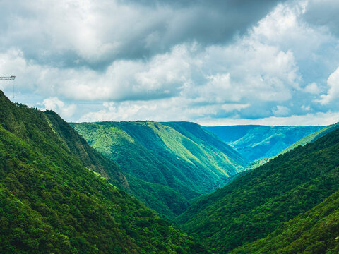 Lush green hills under a dramatic cloudy sky in Cherrapunjee, Meghalaya, showcasing the region&rsquo;s pristine natural beauty and deep, misty valleys.