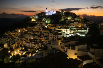 Casares pueblo glows at dusk, with its iconic white houses climbing the hillside and the illuminated castle ruins crowning the peak against a fading twilight sky