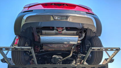 Back side of a new car with exhaust system. View from below. Blue sky background.