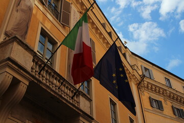 Italian and European union flag on a building with blue cloudy sky background 