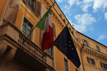 Italian and European union flag on a building with blue cloudy sky background 