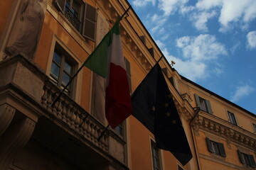 Italian and European union flag on a building with blue cloudy sky background 