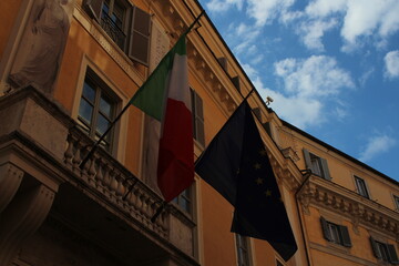 Italian and European union flag on a building with blue cloudy sky background 
