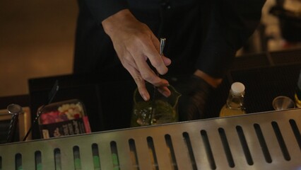 Cropped closeup hand bartender mixing ingredients Midori sour with lime syrup into mixing glass...