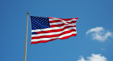 American flag waving against a clear blue sky with a few wispy clouds visible in the background