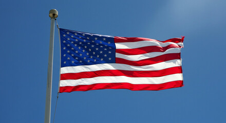 Fototapeta premium A waving american flag against a clear blue sky on a silver pole with a golden ball on top of the pole
