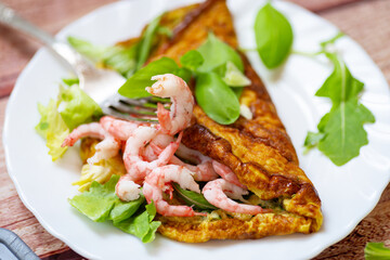 Fried omelette with shrimps and greens on a wooden table