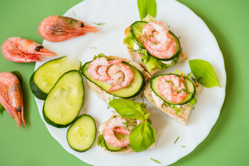 Small canapes with shrimps, salad and cucumbers on a green background