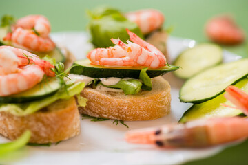 Appetizing appetizers with shrimps, sauce and cucumbers on a green background