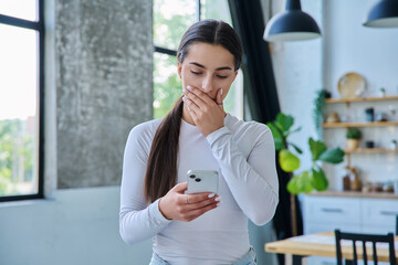Young sad stressed woman standing at home using smartphone