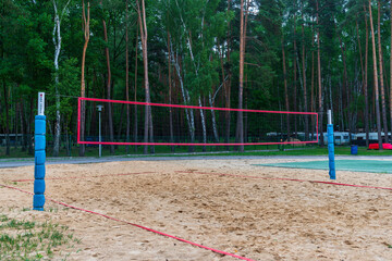A sandy beach volleyball court set against a backdrop of tall pine trees, offering an inviting...