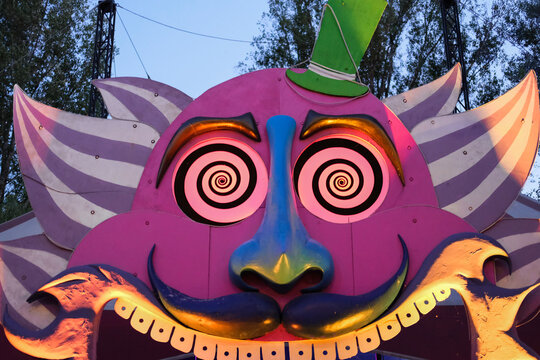 Surreal entrance to a funfair attraction with a colorful, hypnotic face featuring spiral eyes and exaggerated features.